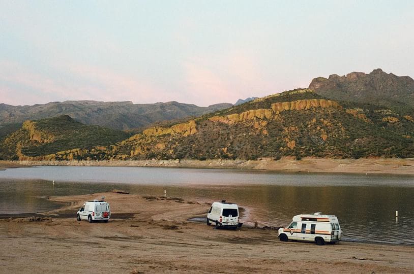 Three campervans near a lake with mountains in the background