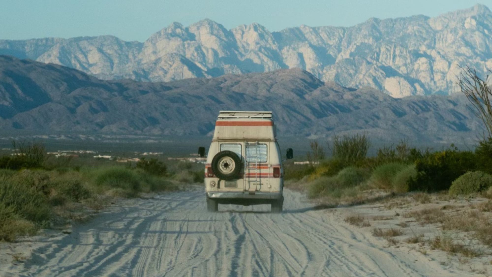 1979 retro van driving on a dusty dirt road toward mountains in the distance at dusk