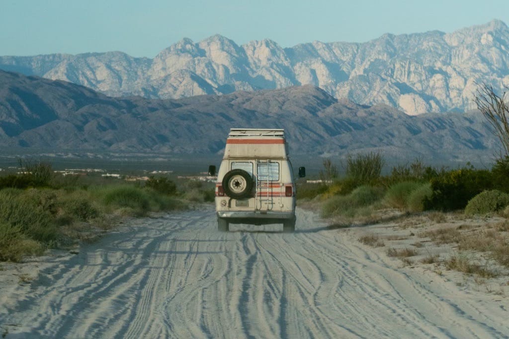 Retro campervan driving on a dusty road surrounded by rugged landscape and mountains in the distance