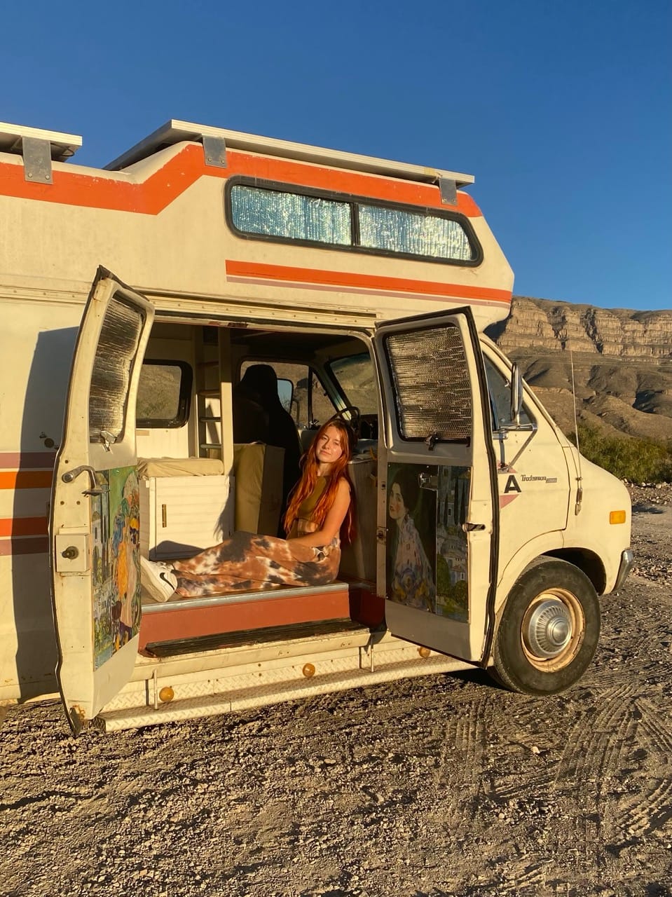 Young woman sitting in a retro van at sunset