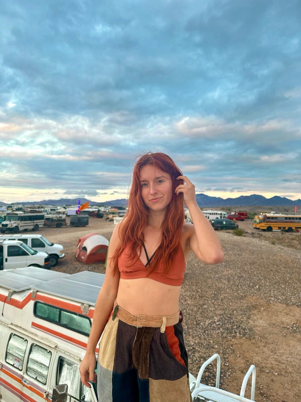 Young woman standing on top of a campervan surrounded by vans and buses